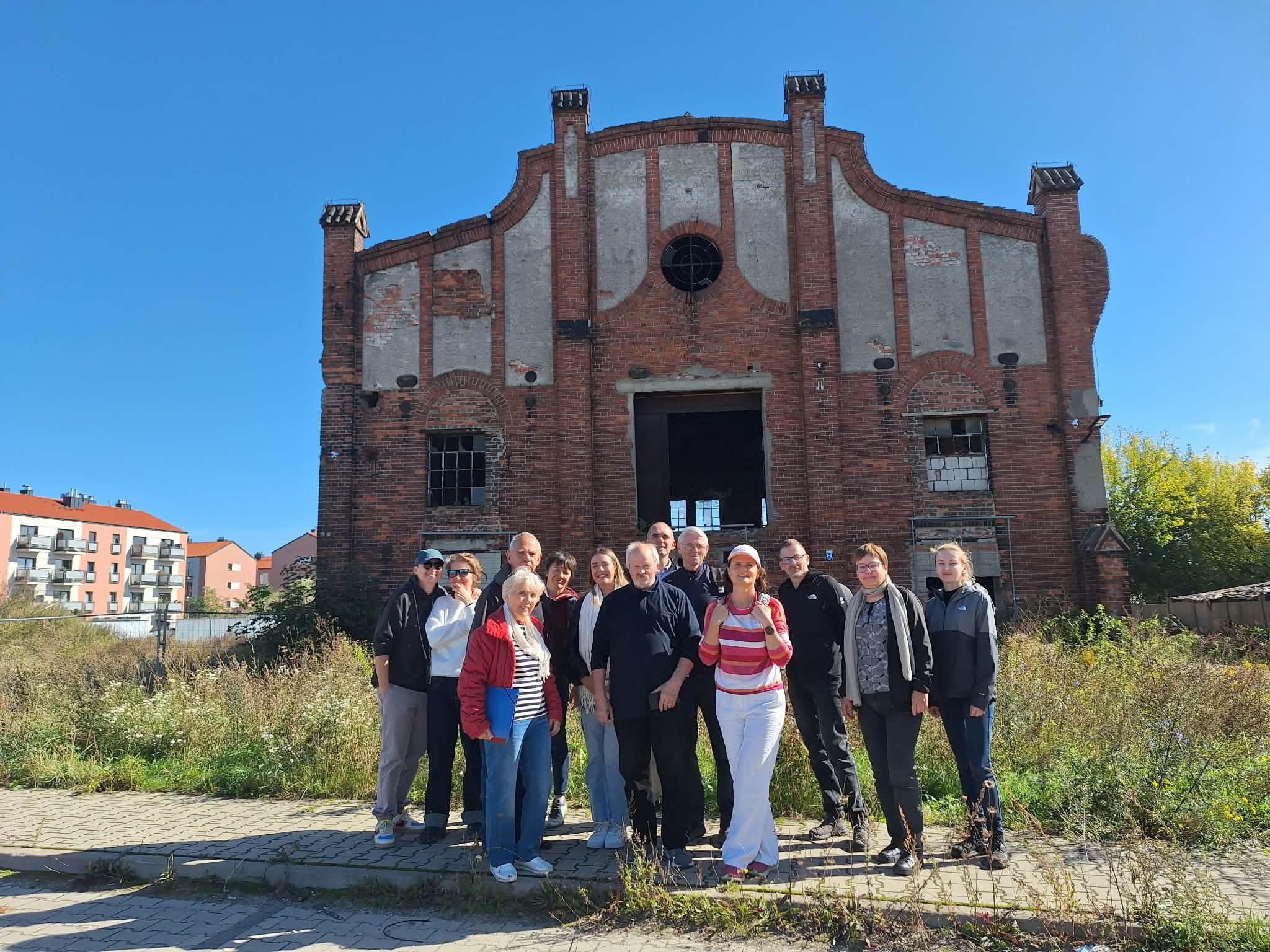Szlak Architektury przemysłowej - zdjęcie z wycieczki zorganizowanej przez Ośrodek Kultury w Luboniu zdjęcie przedstawiające grupę ludzi - kobiet i mężczyzn - na tle starego, zniszczonego budynku z cegły