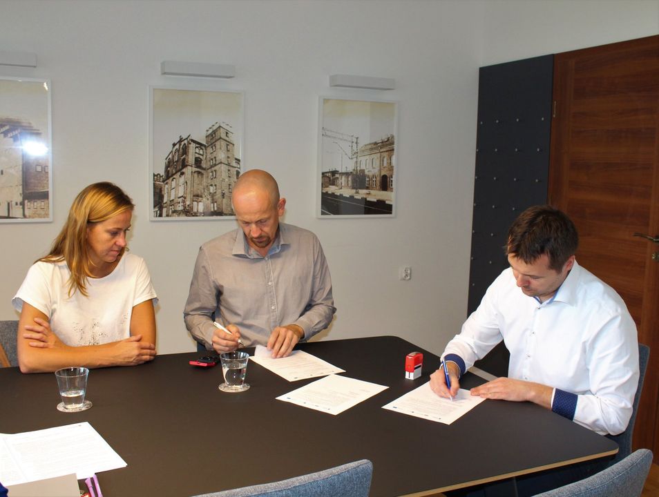 umowę na zagospodarowanie terenu Parku Papieskiego. Na zdjęciu widać trzy osoby siedzące przy stole i podpisujące dokumenty.